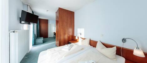 Habitación de hotel con una cama grande, un televisor montado en la pared, un armario de madera y un baño visible a través de una puerta abierta.