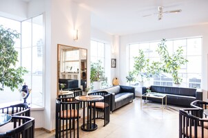 Een ruime woonkamer met een bank, salontafel en stoelen, grote ramen met planten en een plafondventilator.