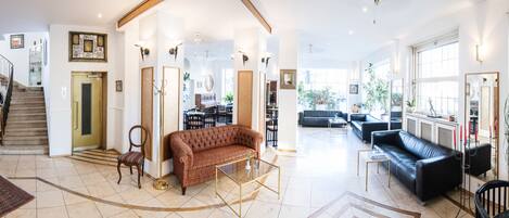 A spacious living area with a brown sofa, a glass coffee table, and a black leather sofa. There is a staircase on the left and a dining area with a table and chairs.