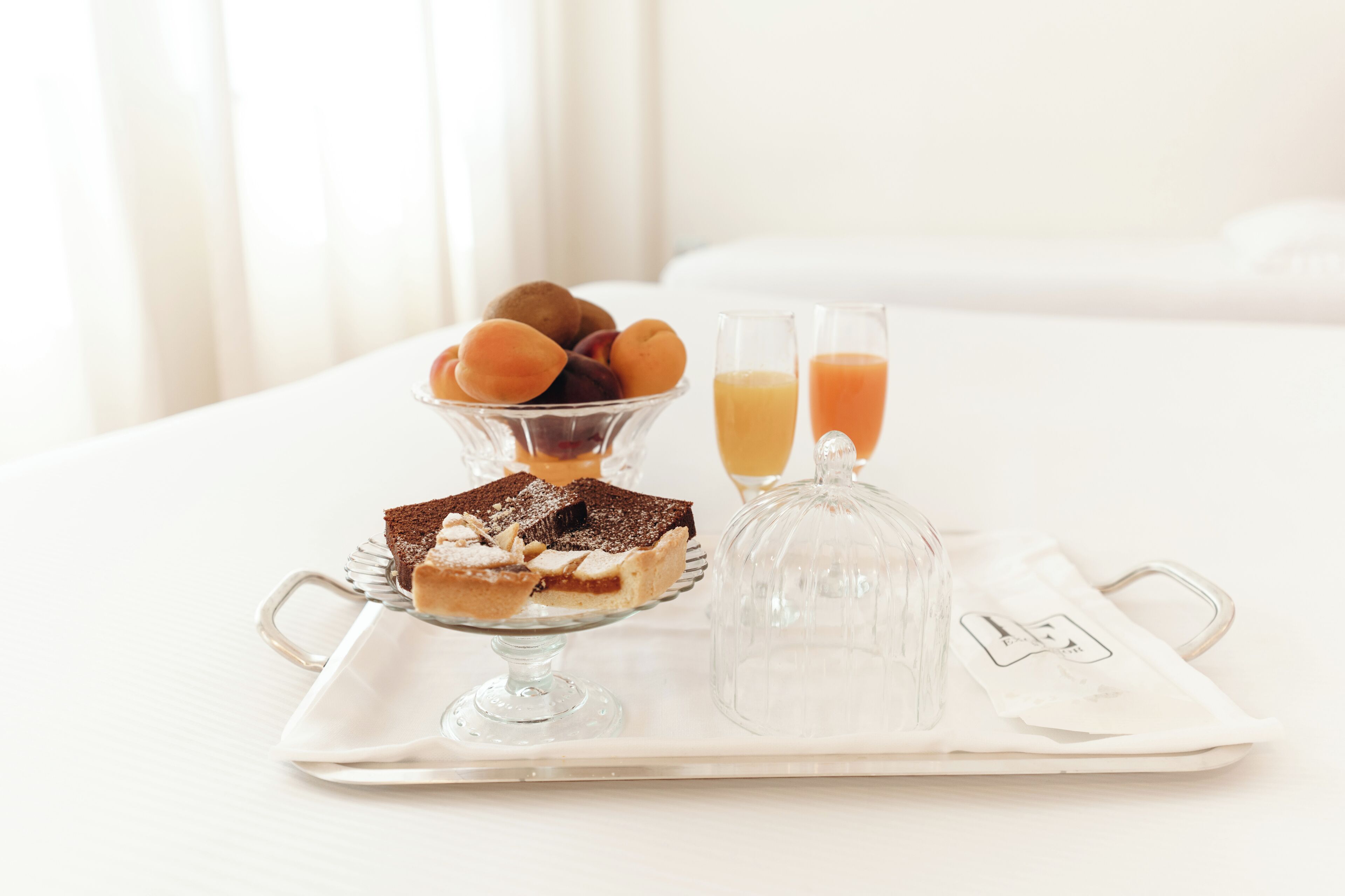 A tray with desserts and juice glasses on a white table in a hotel room.