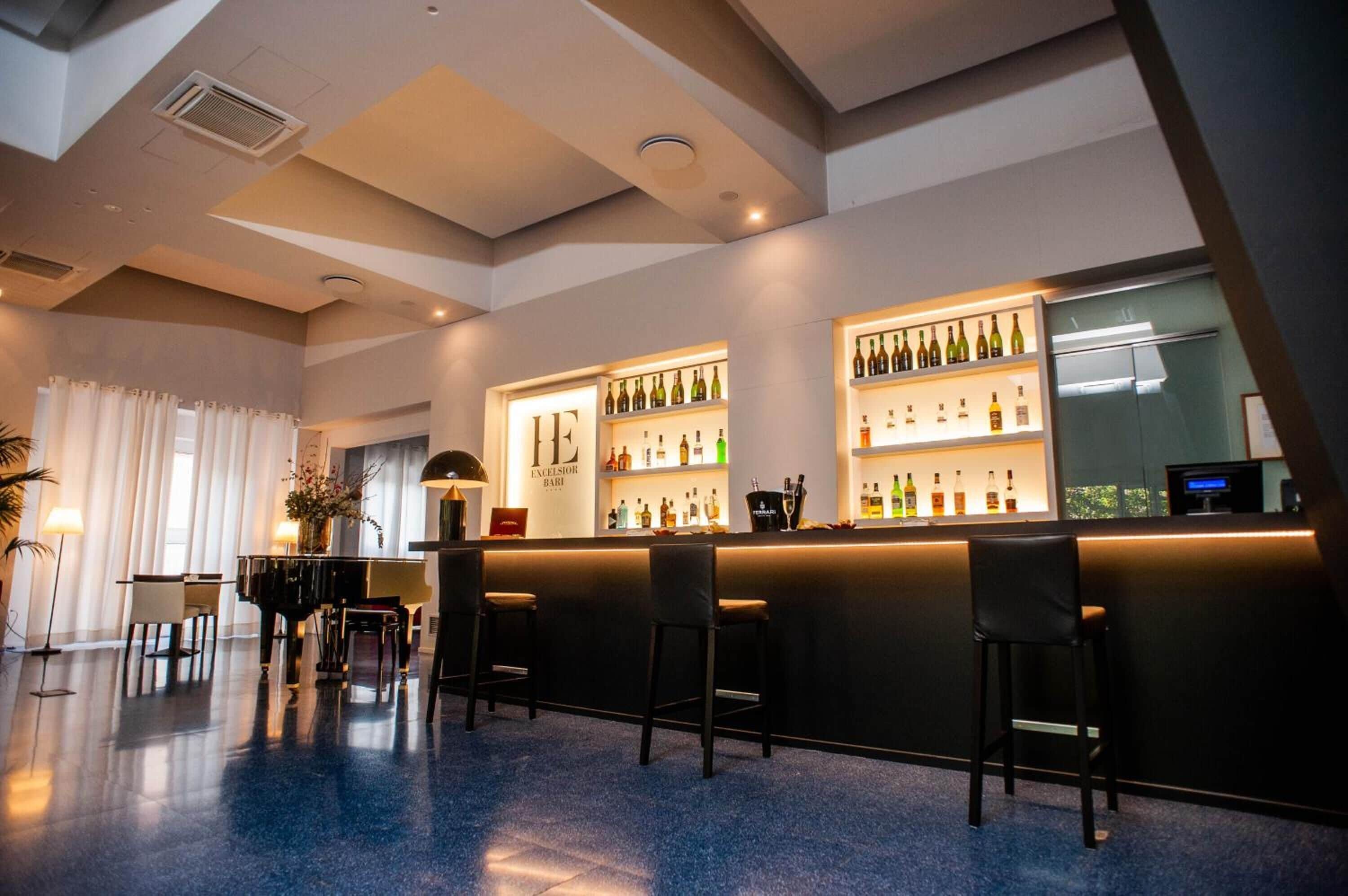 Una zona de bar con un piano, taburetes y estantes llenos de botellas de licores.