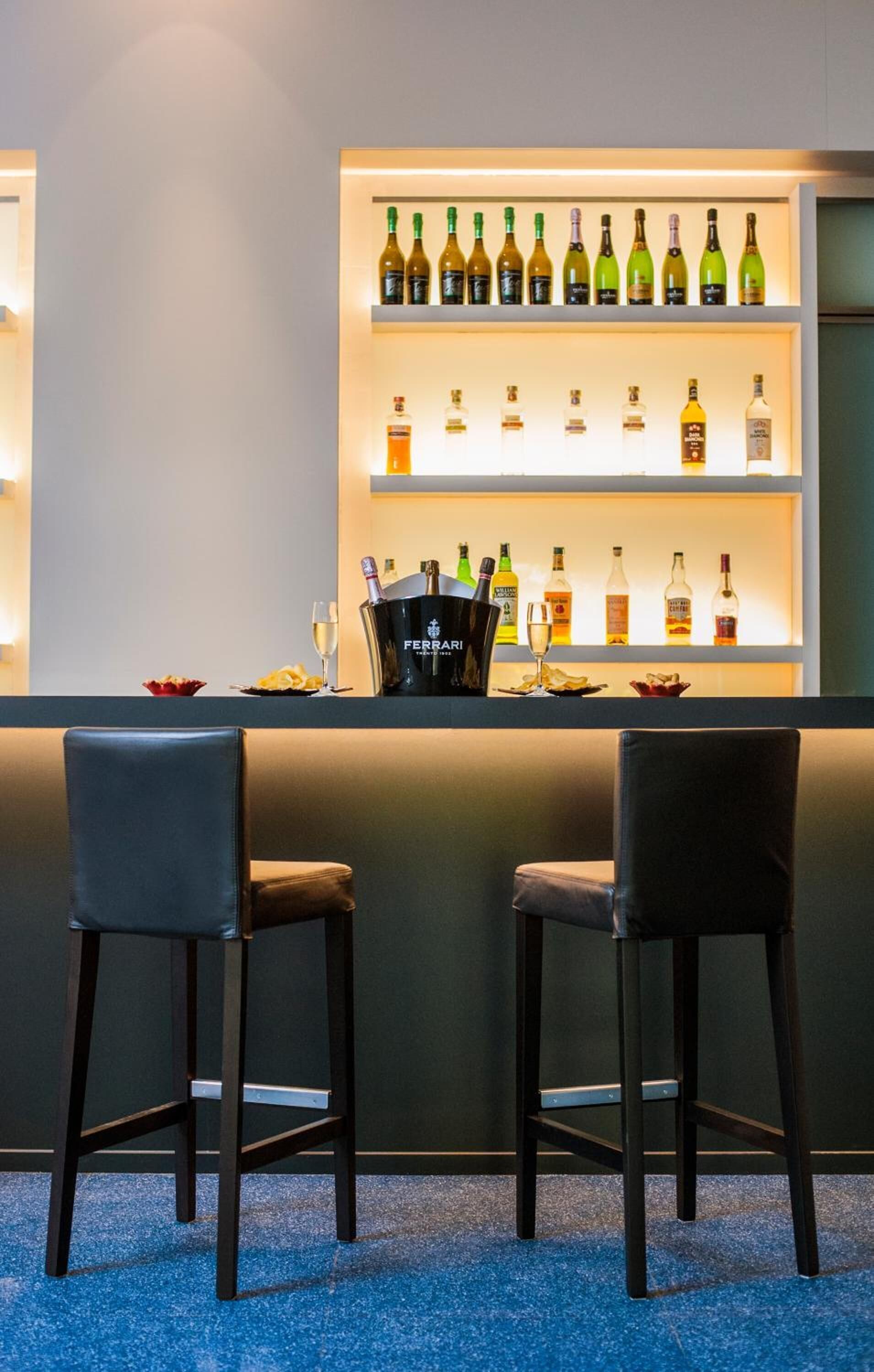 A bar area with two chairs, a bar counter, and shelves of various bottles.