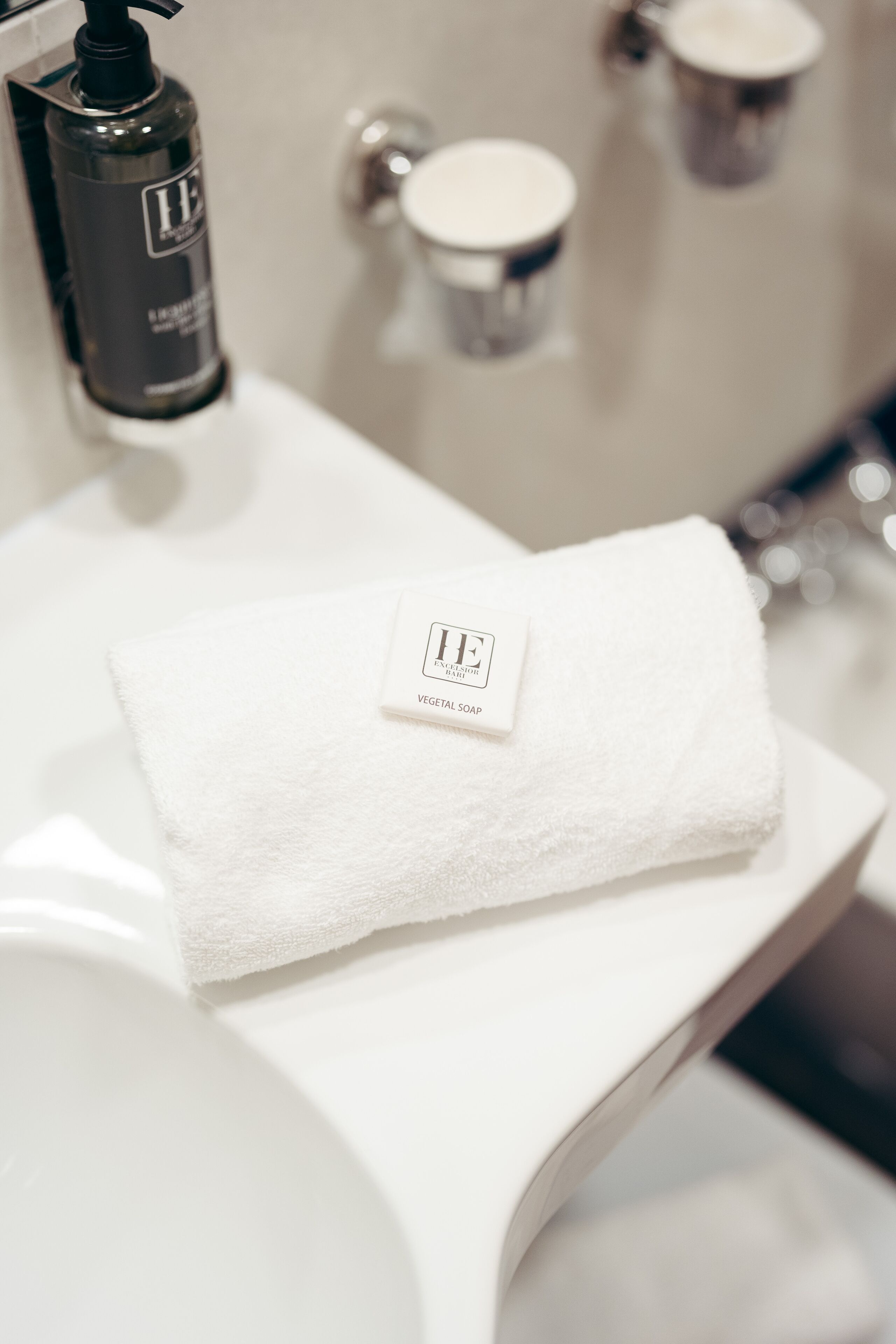 A bathroom with a white towel on a sink, a bottle of liquid soap, and a metal faucet.