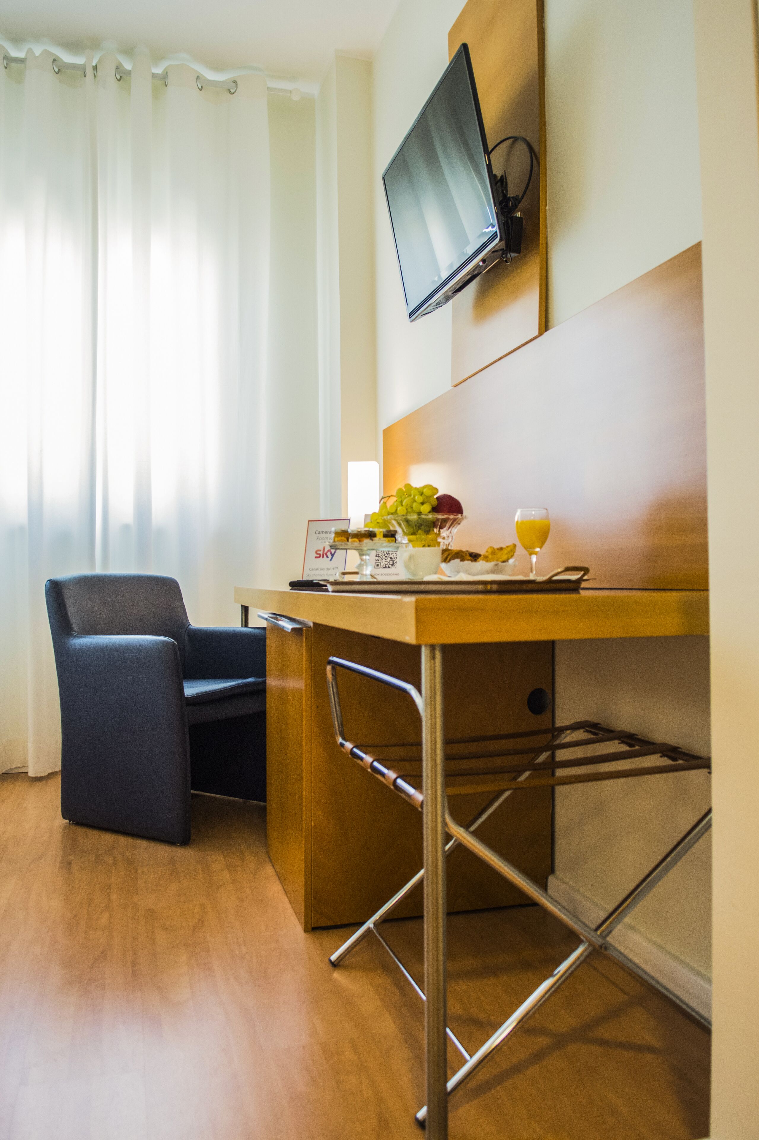 A hotel room with a desk, chair, and a flat-screen TV mounted on the wall.
