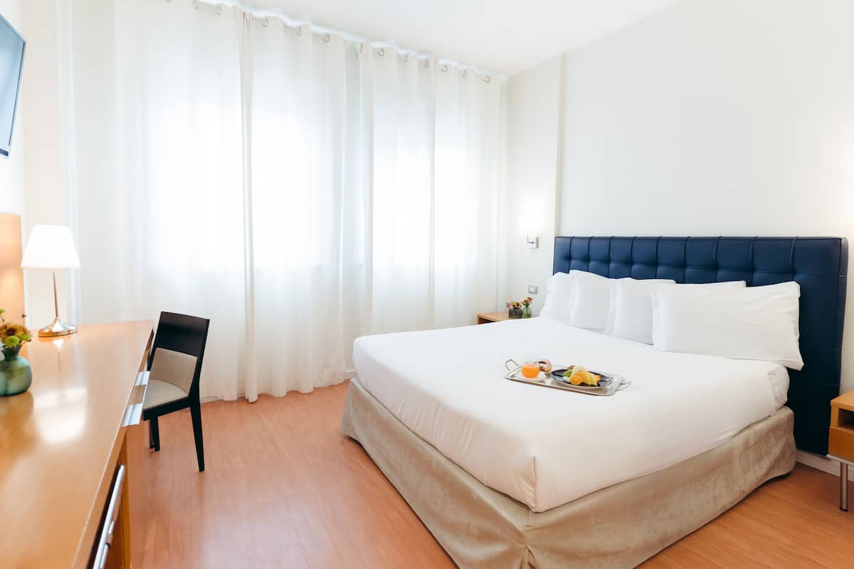 Ein Hotelzimmer mit Bett, Sessel, Tisch und einem Tablett mit Frühstücksartikeln.