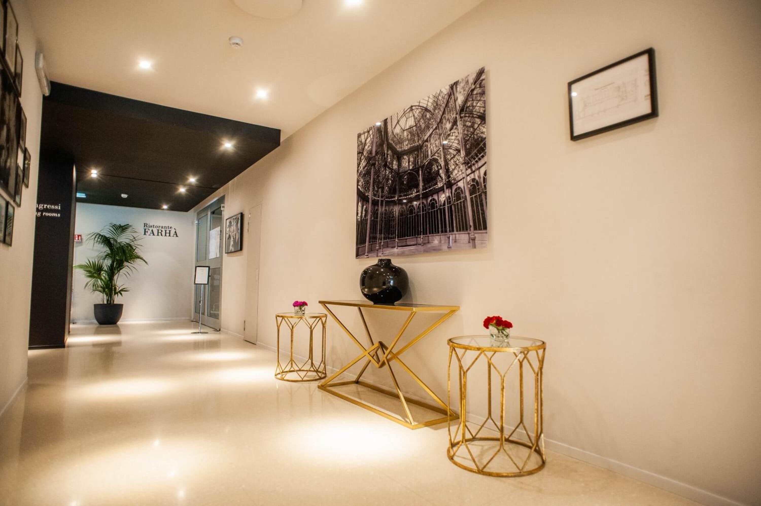 A modern hotel lobby with a polished floor, a large framed architectural drawing, and a potted plant.