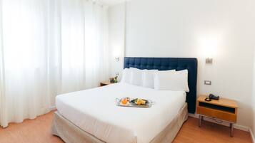 Un lit bien fait, avec un plateau de petit-déjeuner à proximité, une table de chevet avec une lampe et une fenêtre avec des rideaux.