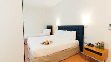 Habitación de hotel con una cama grande, una mesita de noche con lámpara y una bandeja de fruta sobre la cama.