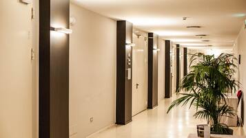 A modern hotel corridor with a long hallway, doors, and a potted plant.