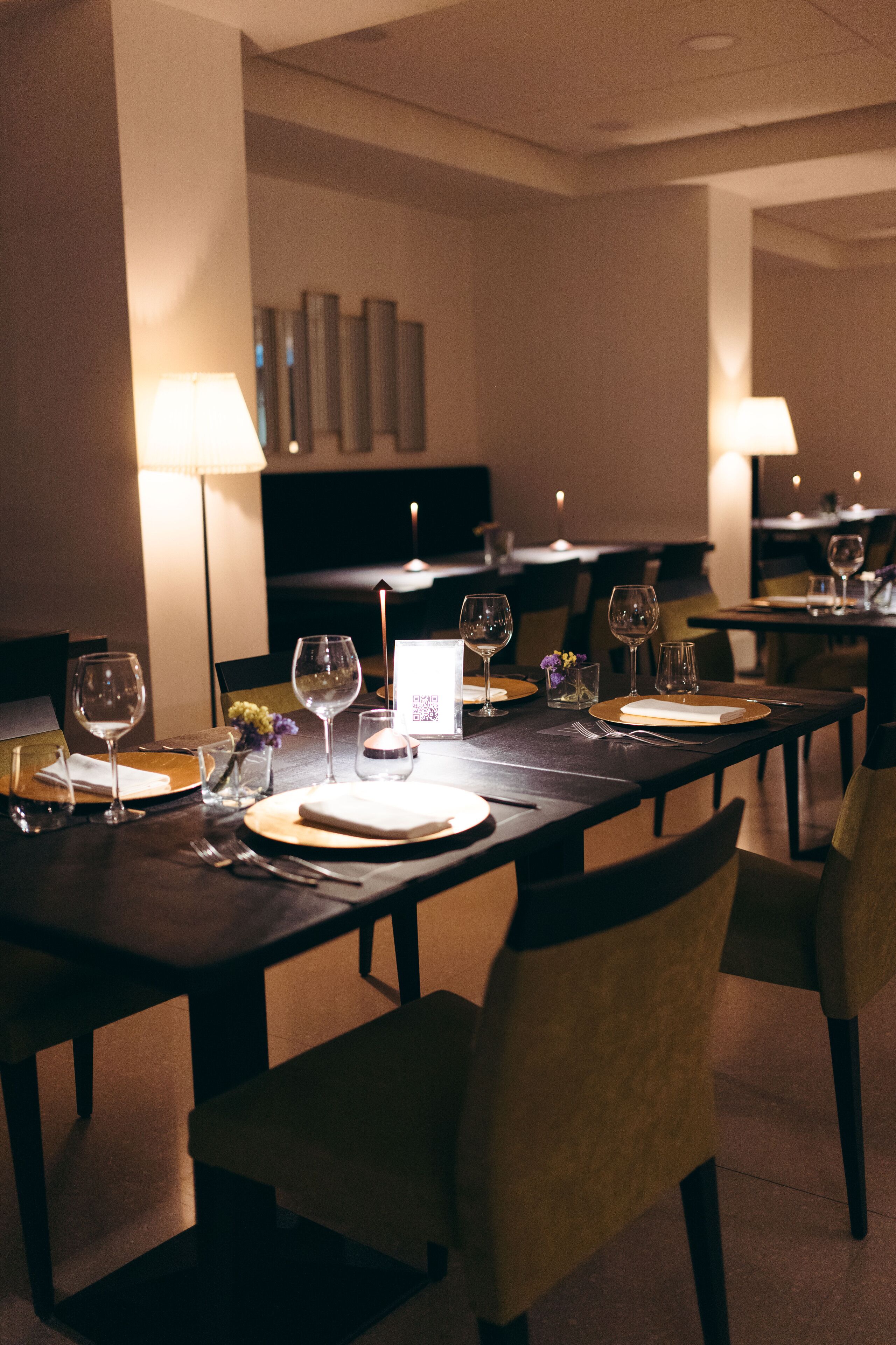 A dining area with tables set for two, equipped with wine glasses, plates, and cutlery.