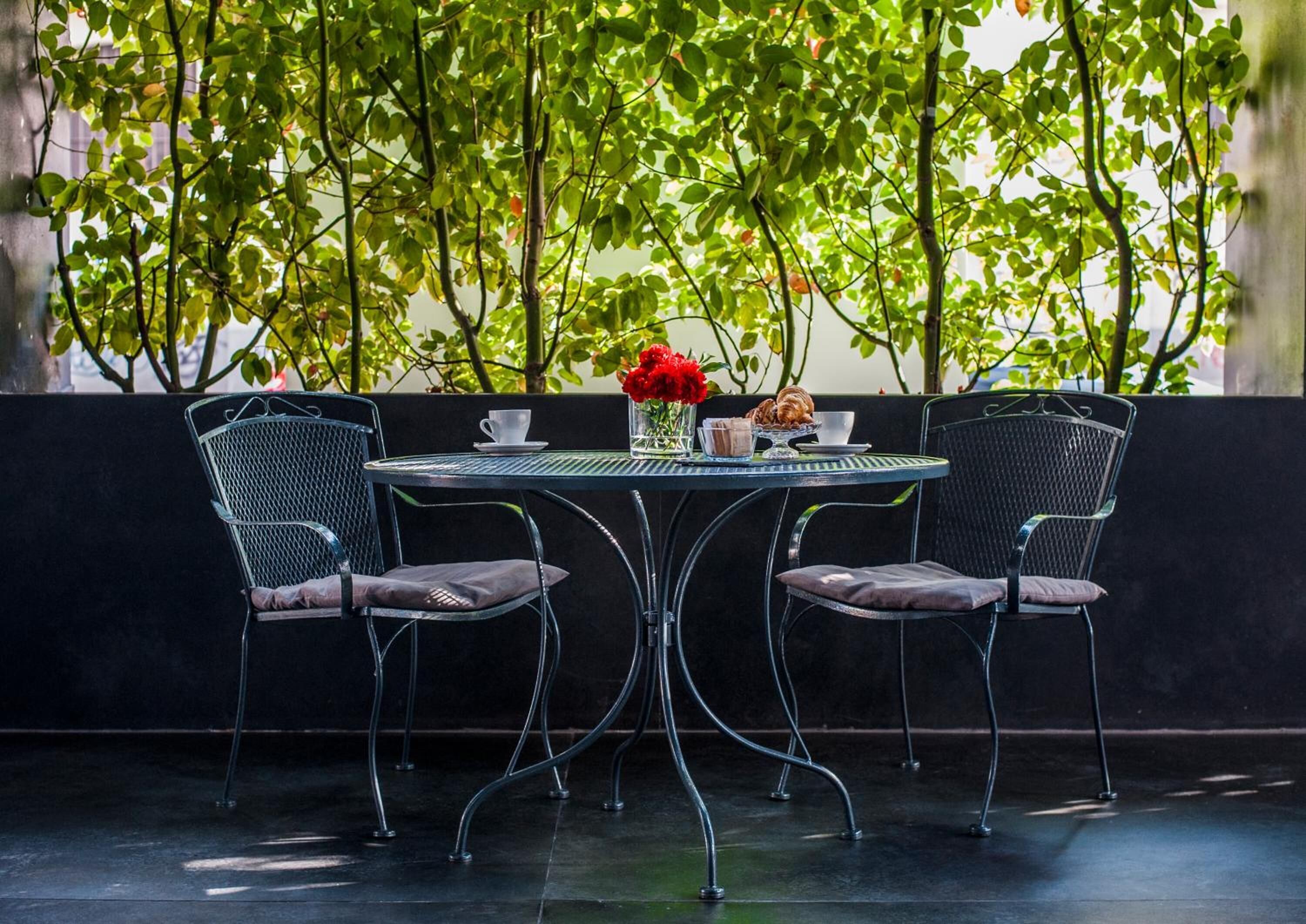 A table with two chairs, a vase with red flowers, and a plate of pastries.
