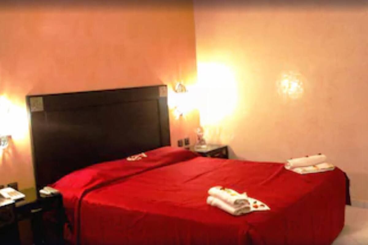 A hotel room with a bed, a nightstand, a lamp, and a door.