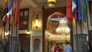 A hotel lobby with multiple flags, a chandelier, and a staircase leading to an upper level. - Hotel Mont Gueliz (Marrakech)