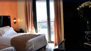 A hotel room with two beds, a nightstand, a lamp, and a view of the outside. - Hotel Mont Gueliz (Marrakech)