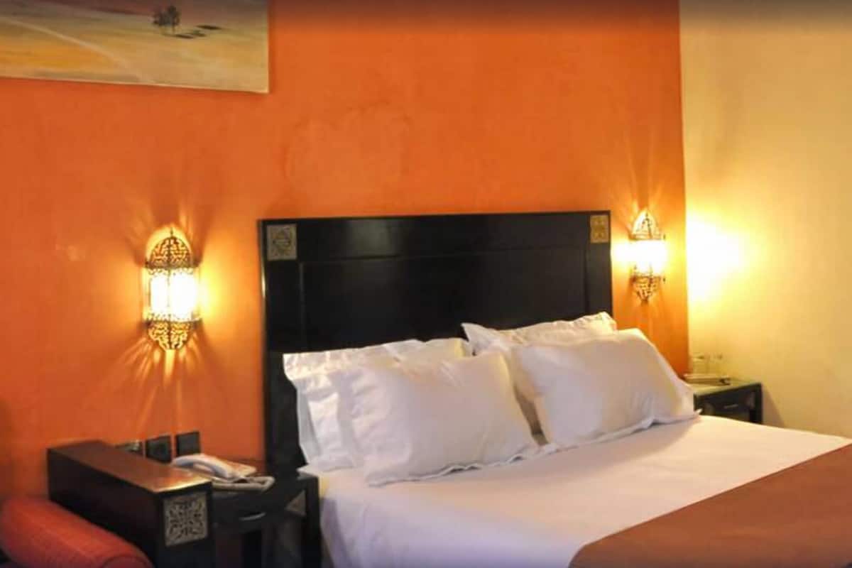A hotel room with a large bed, two bedside lamps, a nightstand, and a red chair.