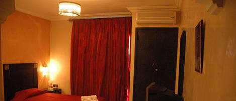 Quarto de hotel com duas camas, uma escrivaninha, uma cadeira, uma televisão e cortina vermelha.