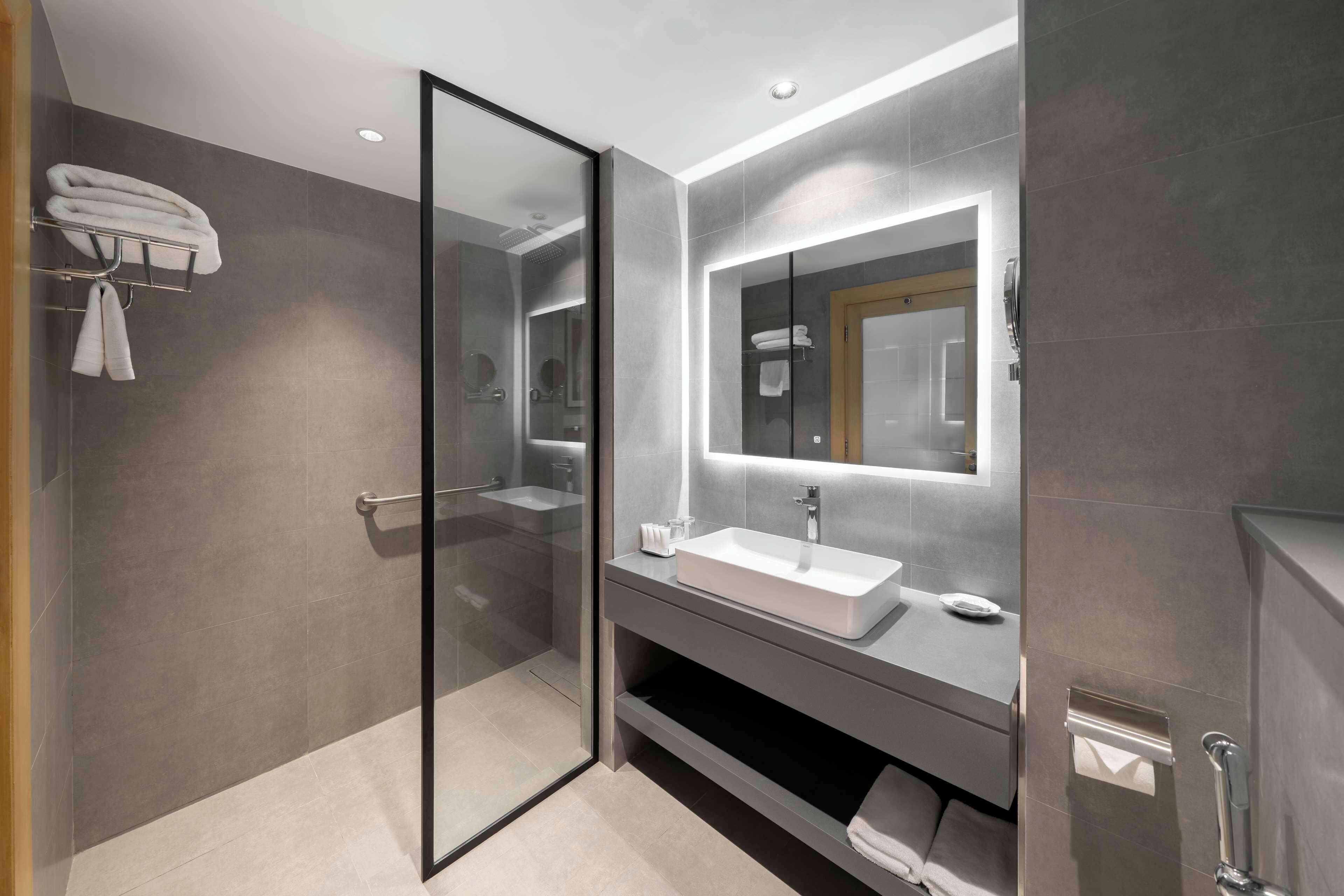 Un baño moderno con cabina de ducha de vidrio, un espejo grande y un lavabo con tocador.