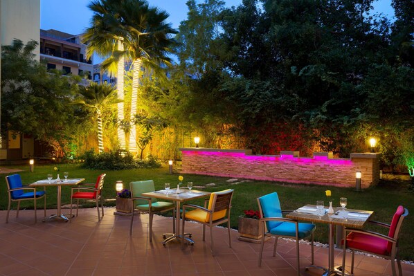 An outdoor dining area with multiple tables and chairs, surrounded by lush greenery and decorative lighting. - Radisson Hotel Al Khobar (Al Khobar)