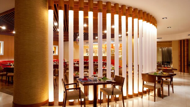 A modern dining area with a central table surrounded by chairs, a wooden column, and a decorative partition with vertical slats.