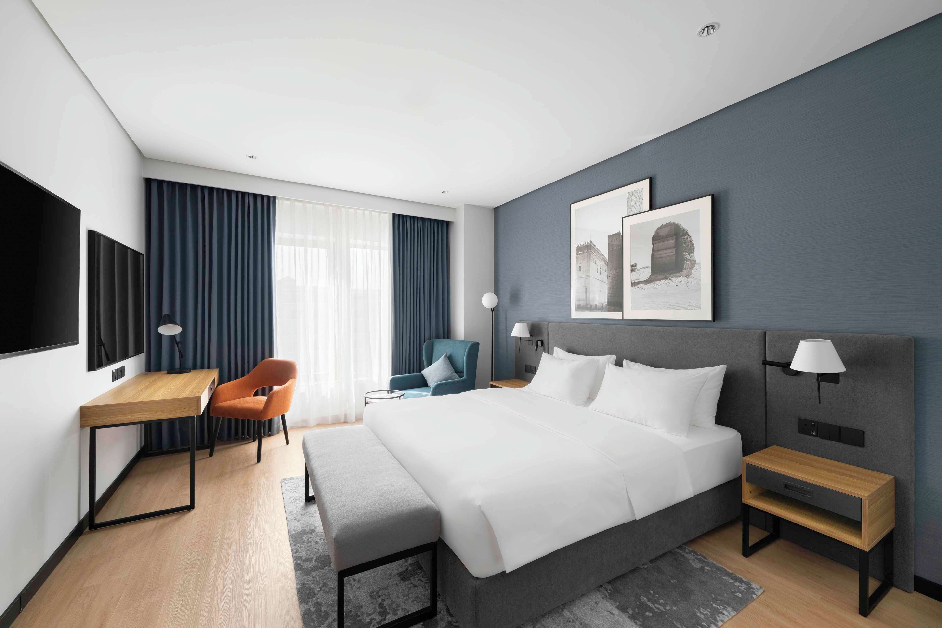 Una habitación de hotel moderna con una cama grande, un escritorio, una silla y un televisor.
