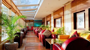 A spacious indoor area with a long row of red leather chairs and tables, large windows, and potted plants.