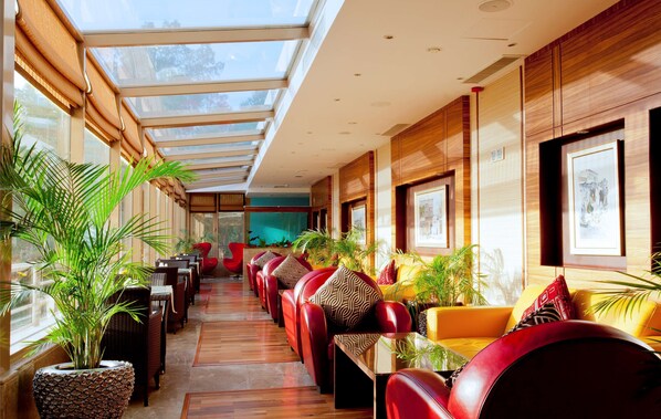 A spacious indoor area with a long row of red leather chairs and tables, large windows, and potted plants. - Radisson Hotel Al Khobar (Al Khobar)