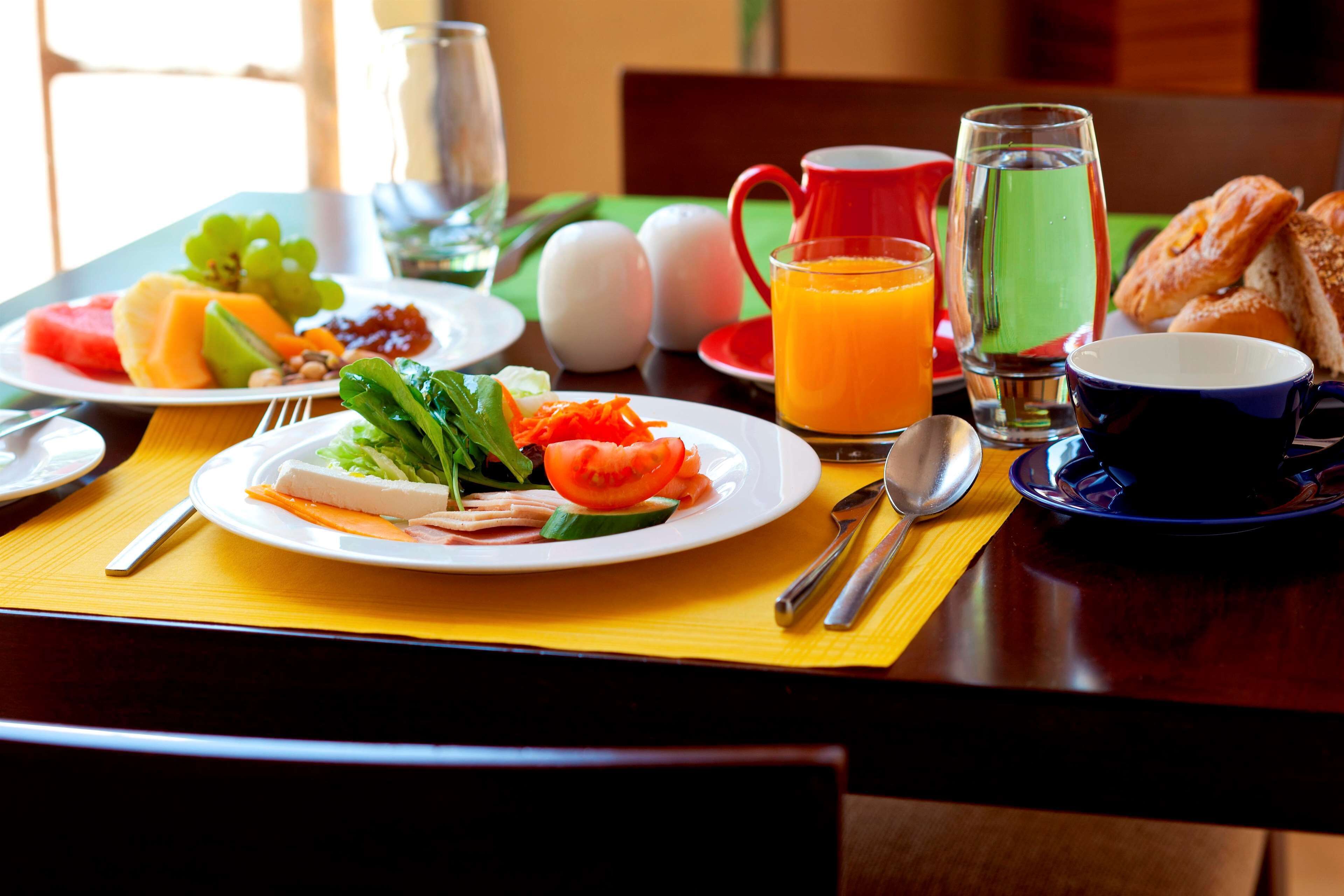 Una mesa de desayuno con platos de comida, una jarra de jugo de naranja, un vaso de agua y una taza de café.