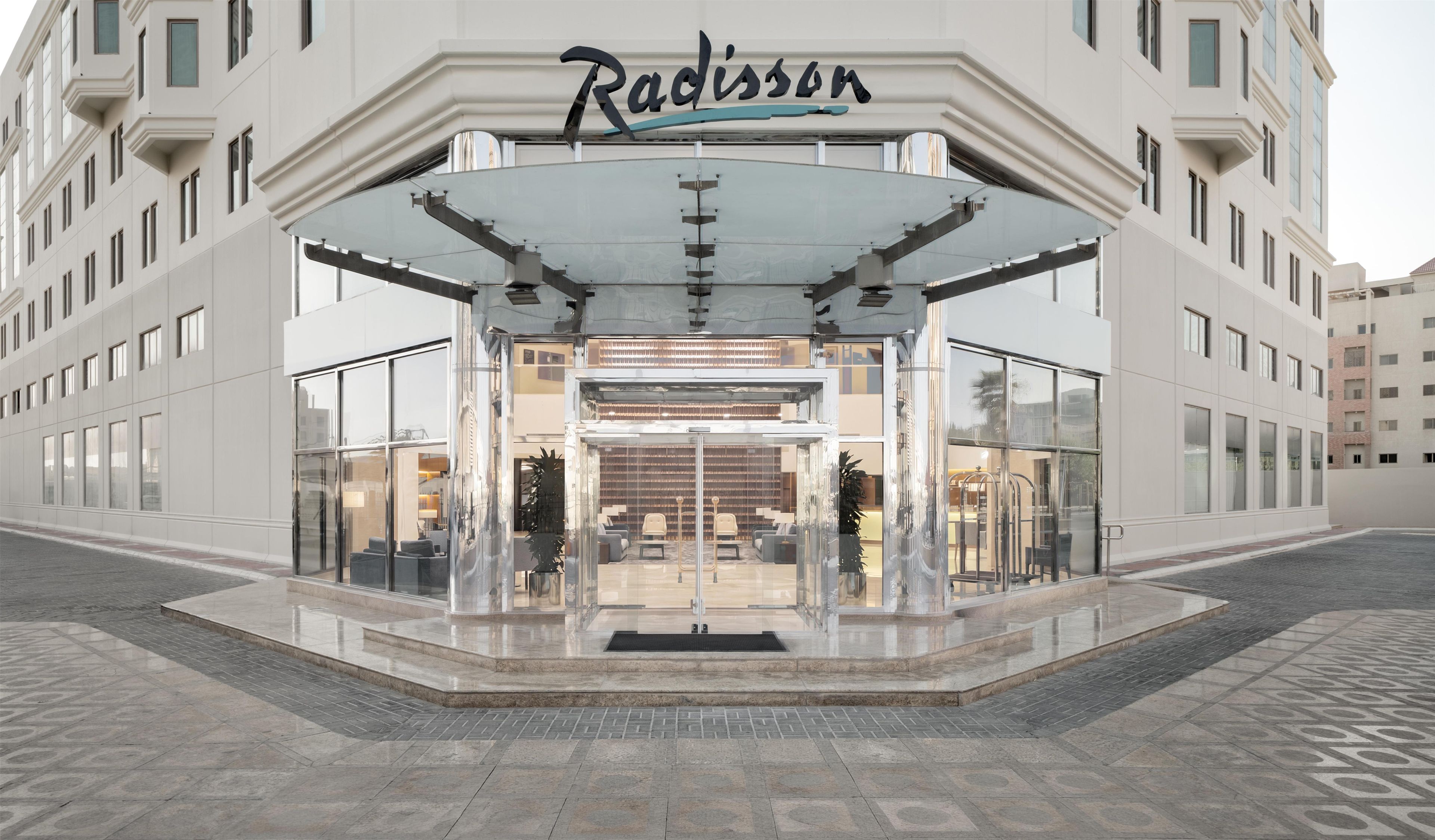 Entrada de un hotel Radisson con fachada de vidrio, vestíbulo cubierto y pavimento de baldosas.