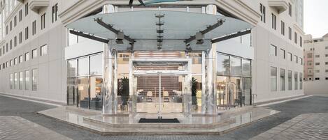 Entrada de un hotel Radisson con fachada de vidrio, vestíbulo cubierto y pavimento de baldosas.