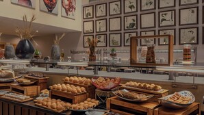 Buffet com diversos produtos de panificação e doces dispostos em caixas e recipientes de madeira.