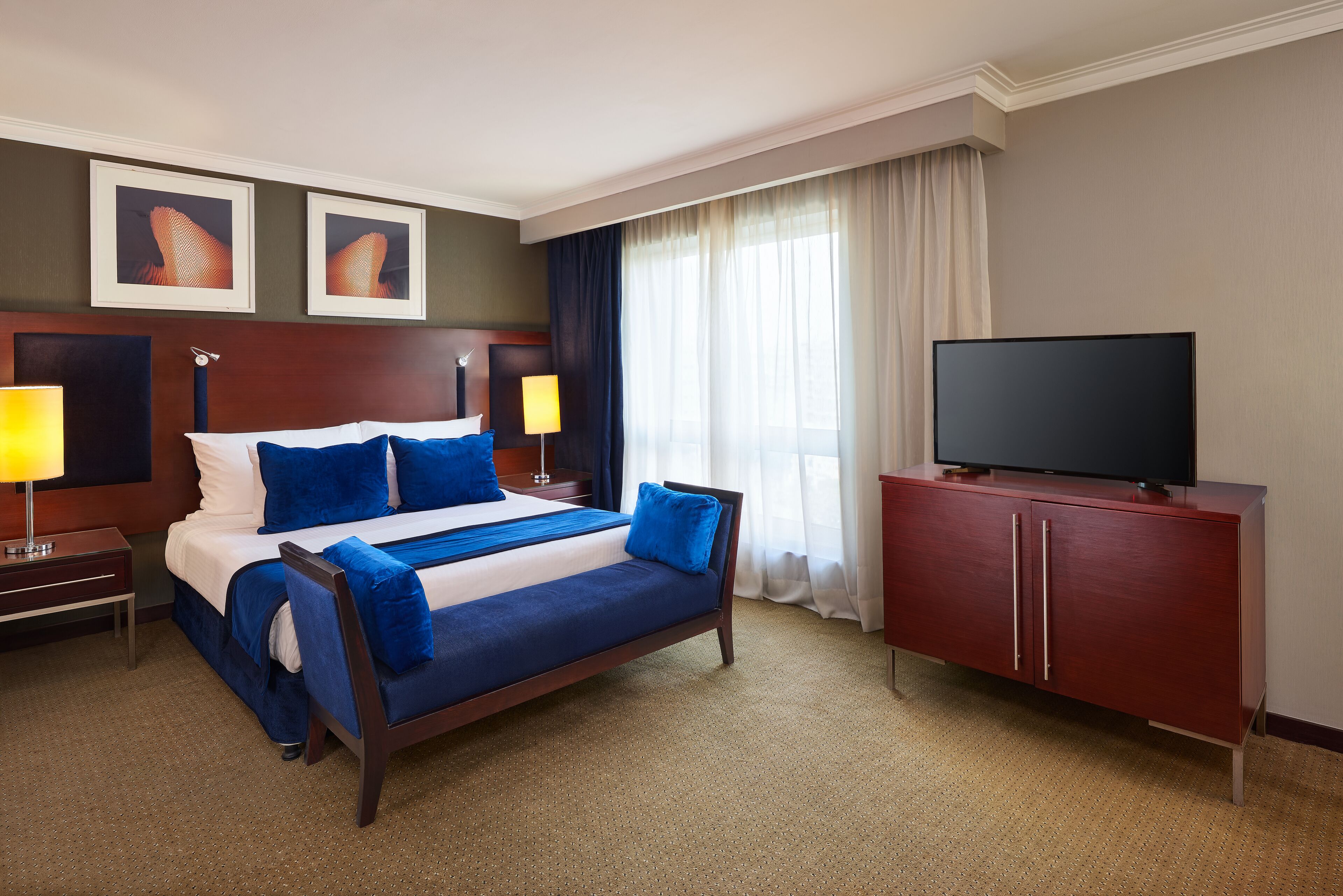 Une chambre d’hôtel avec un grand lit, un téléviseur posé sur un meuble et deux tableaux encadrés accrochés au mur.