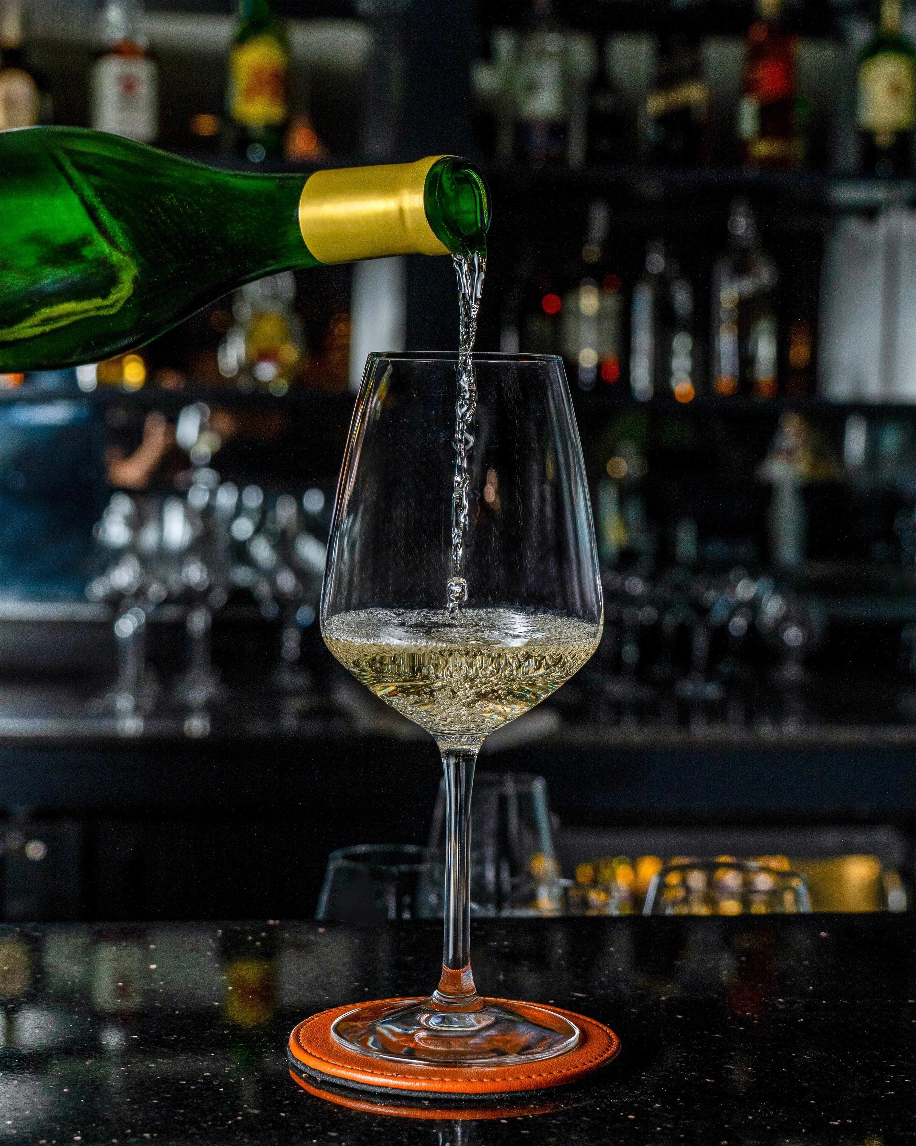 A glass of white wine being poured from a green bottle.