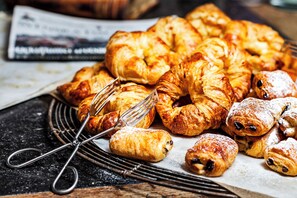A variety of pastries on a wire rack, including croissants and other baked goods, with a newspaper in the background.