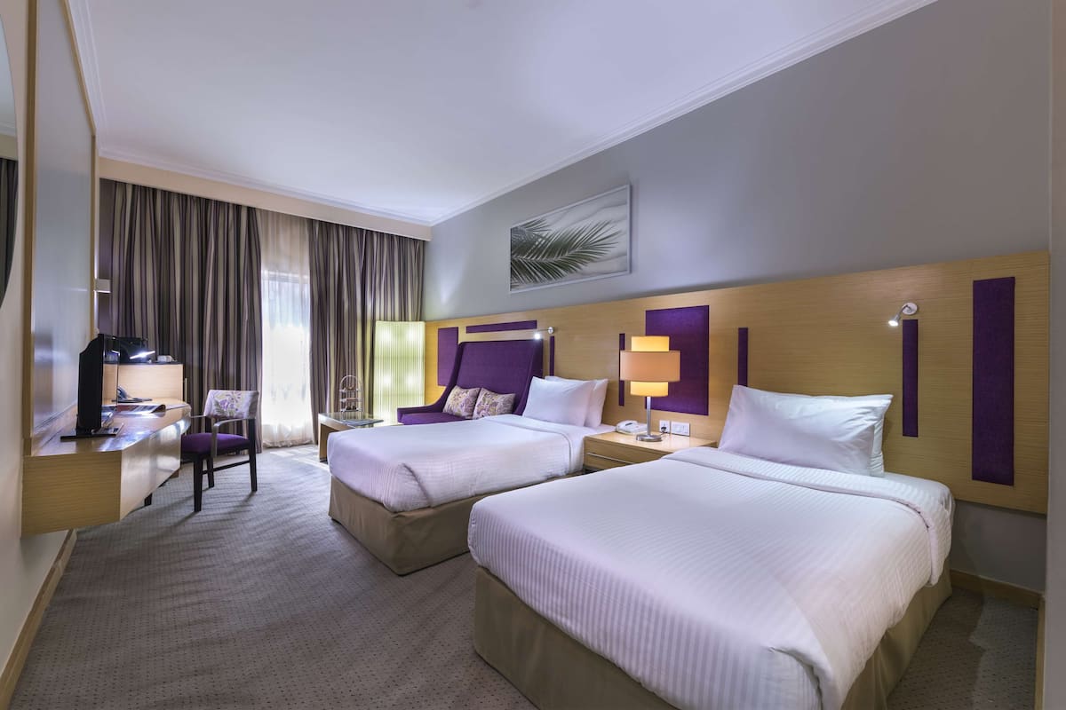 A hotel room with two beds, a desk, a chair, and a television.