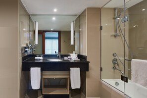 Un baño moderno con ducha envuelta en vidrio, un lavabo sobre encimera negra y un mueble de tocador de madera.