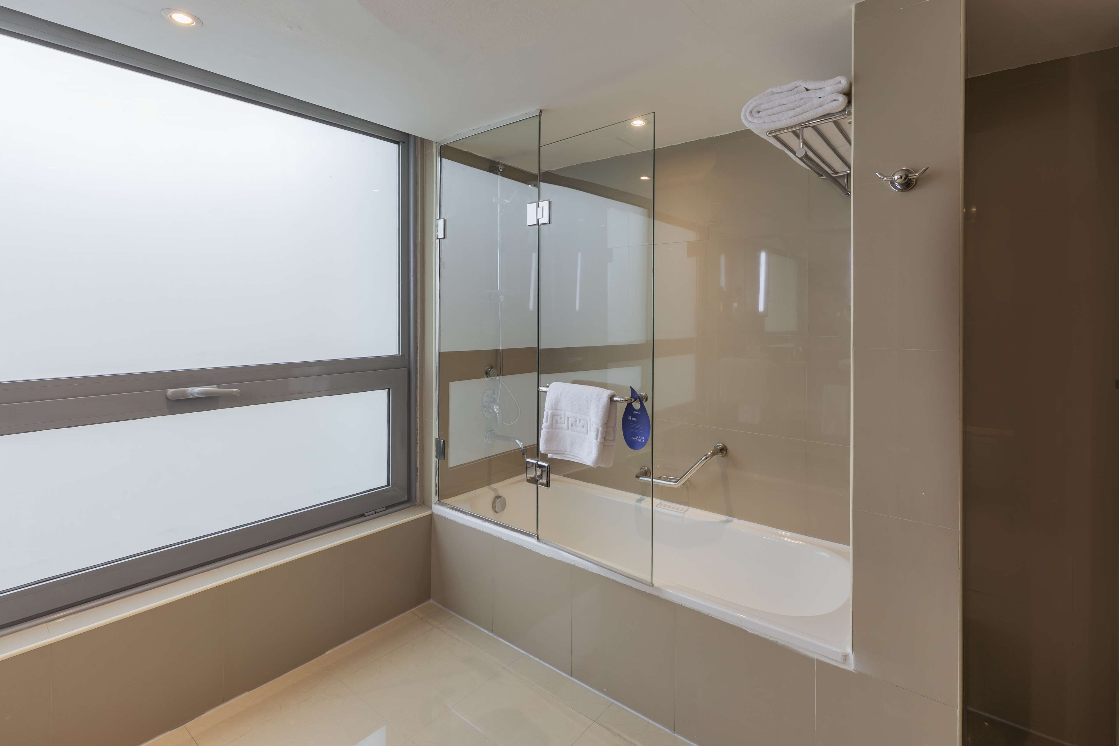 A modern bathroom with a glass-enclosed shower, a bathtub, and a large window.