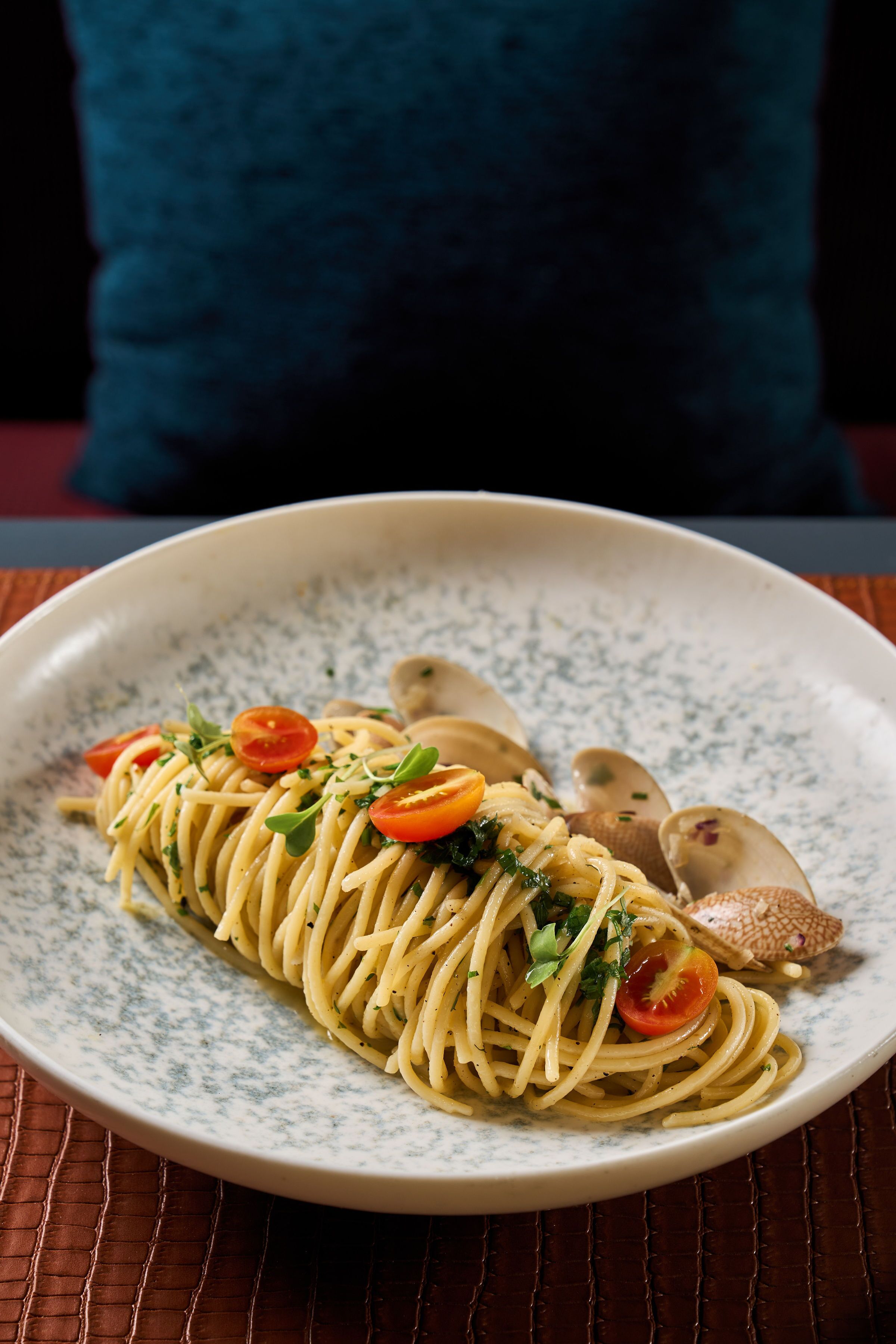 A plate of spaghetti with clams and cherry tomatoes on a speckled plate.