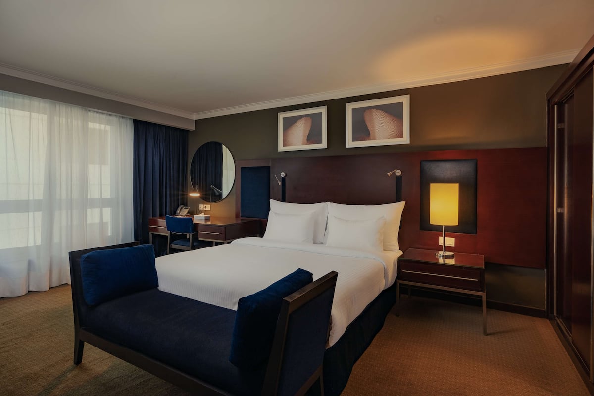 A hotel room with a large bed, a desk, a chair, a lamp, and a mirror.