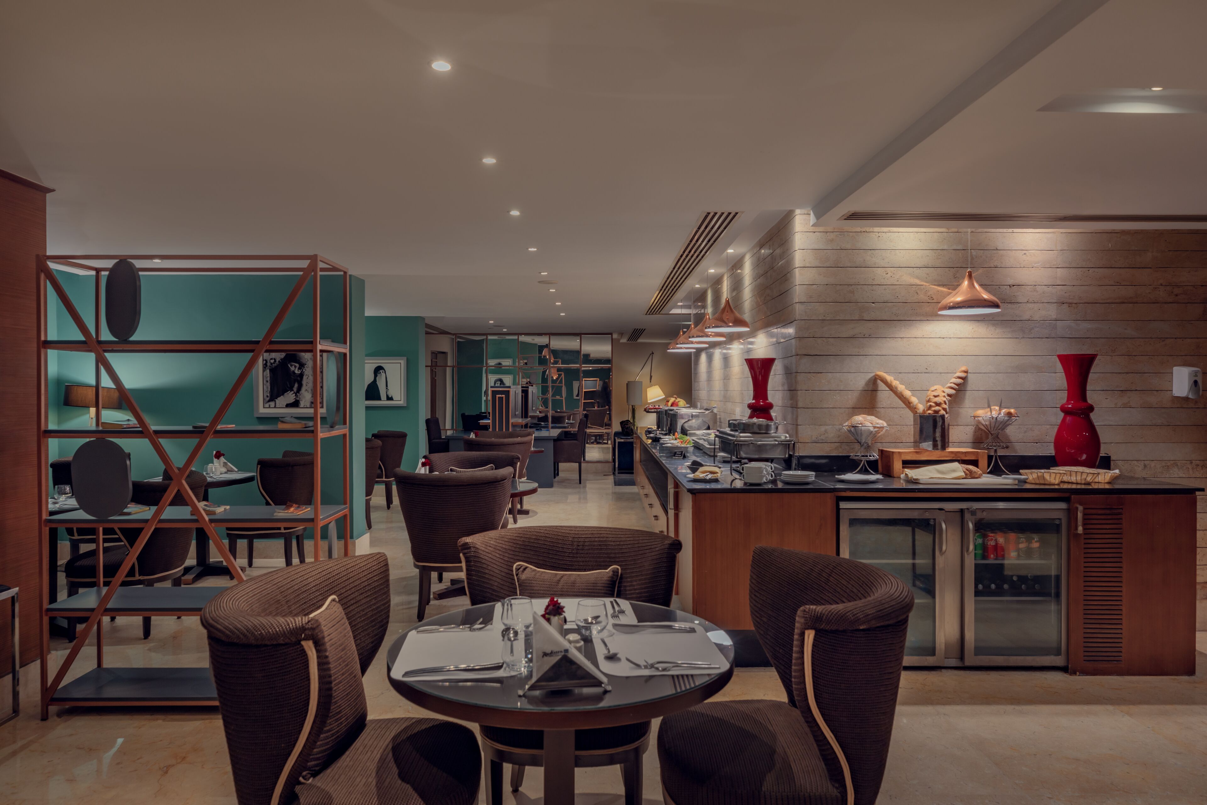 Un espace repas moderne avec une table ronde pour quatre personnes, entourée de chaises en osier. On y trouve également un coin cuisine avec un réfrigérateur et un plan de travail sur lequel sont disposés divers objets.