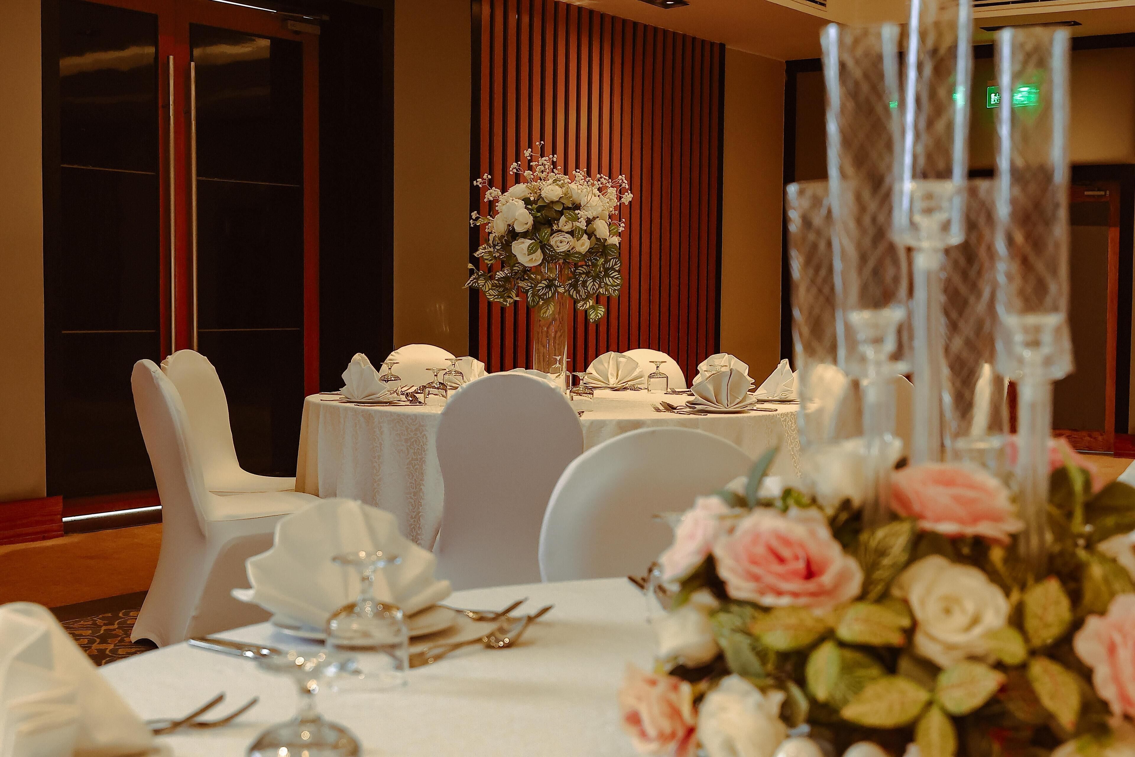 Una mesa de banquete dispuesta con manteles blancos, sillas blancas y centros de mesa florales.