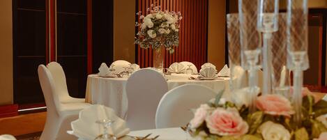 Una mesa de banquete dispuesta con manteles blancos, sillas blancas y centros de mesa florales.
