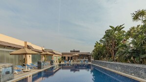 Piscina com espreguiçadeiras e guarda-sóis, cercada por vegetação e um edifício com design moderno.