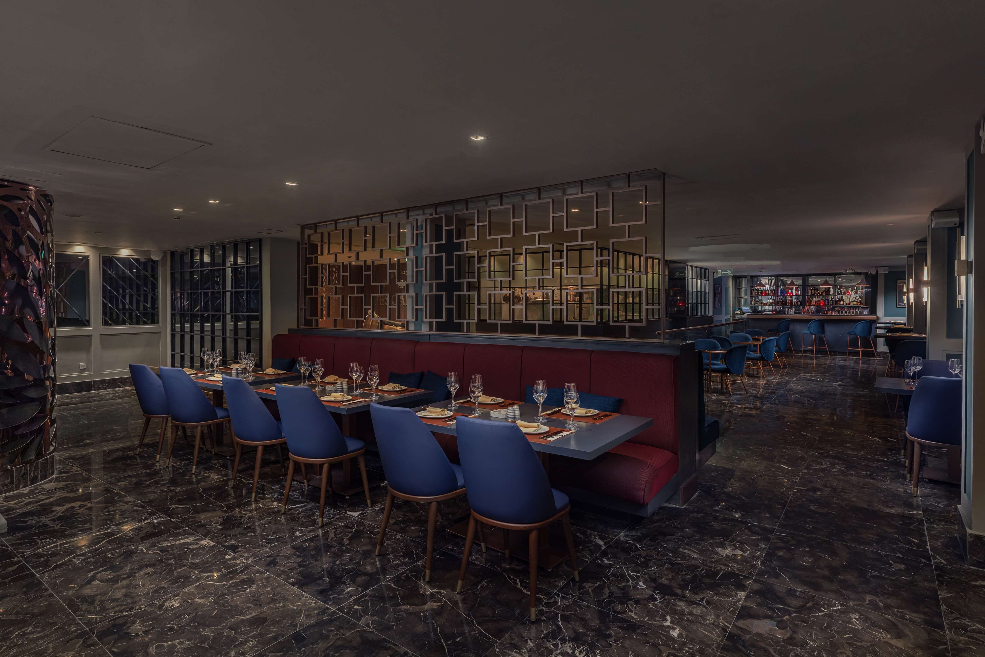 Un restaurante con suelo de mármol, sillas azules y una zona con cabinas rojas.