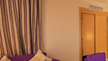 A room with a purple sofa, a glass coffee table, a purple armchair, and a wooden wardrobe.