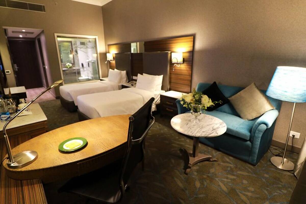 Quarto de hotel com duas camas, uma mesa de jantar, um sofá e uma pequena mesa redonda com um vaso de flores.