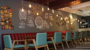 Zona de bar con sillas color turquesa, un banco rojo y una pared decorada con carteles de cerveza y escritura en una pizarra.