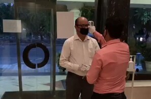 A man in a white shirt and black pants standing in a lobby with a circular sign on the wall and a glass door. - The Piccadily Chandigarh (Chandigarh)