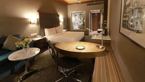 Habitación de hotel con cama, una mesita redonda pequeña, una silla, un sofá y un ventilador de techo.