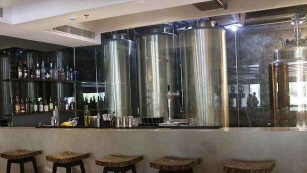 Zona de bar con taburetes y barra, con botellas y copas en estantes.