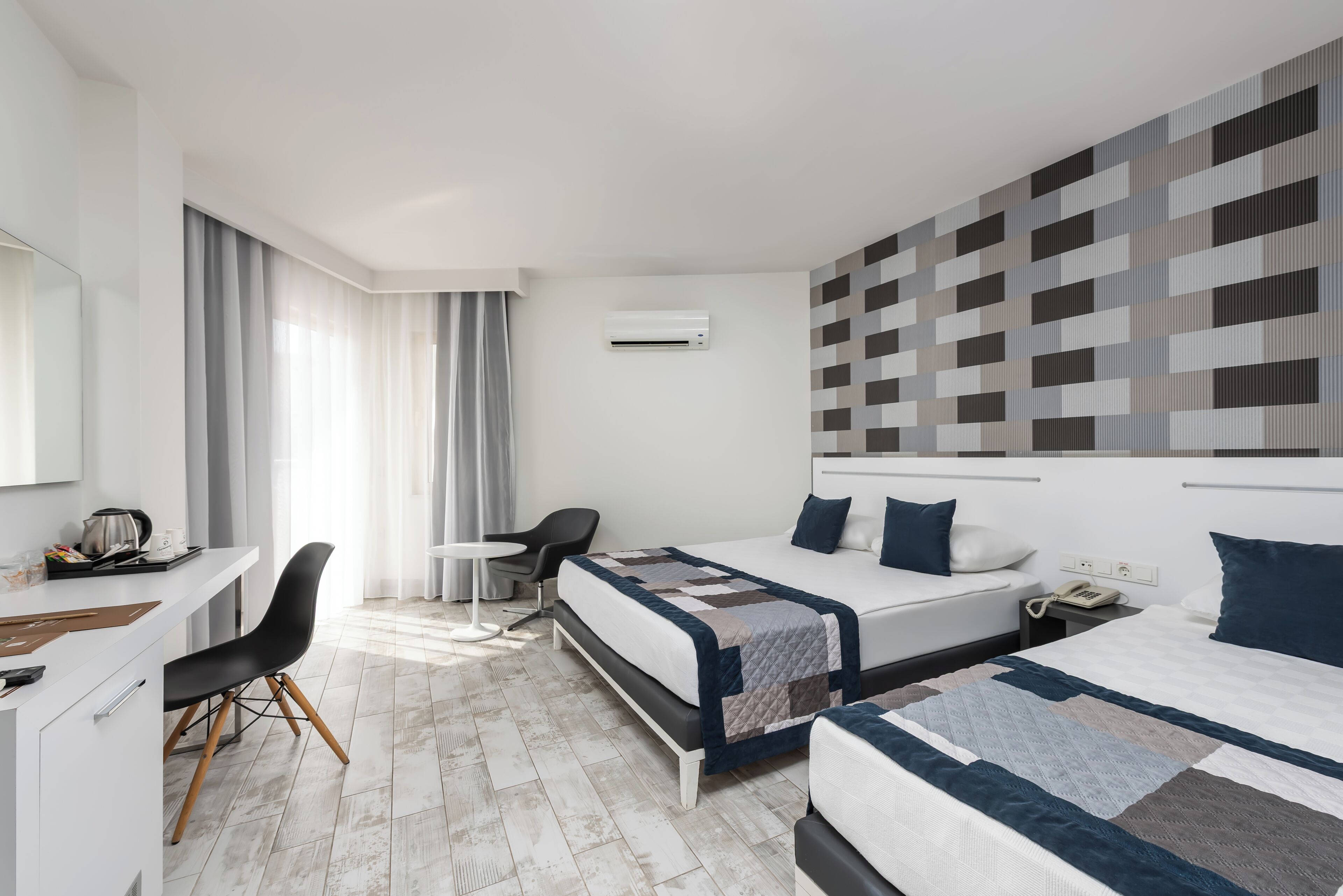 A hotel room with a bed, bedside table, chair, desk, and a large window with curtains.